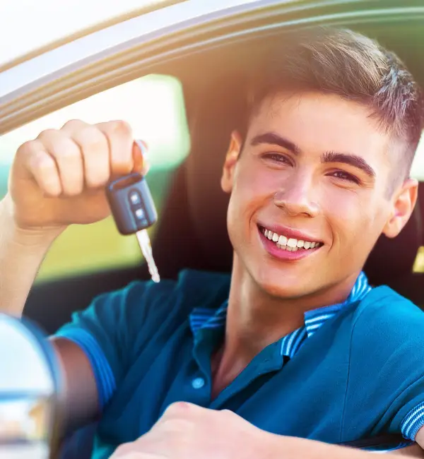 A young man beams with joy as he leans out of his car window, holding up the keys to his brand-new vehicle